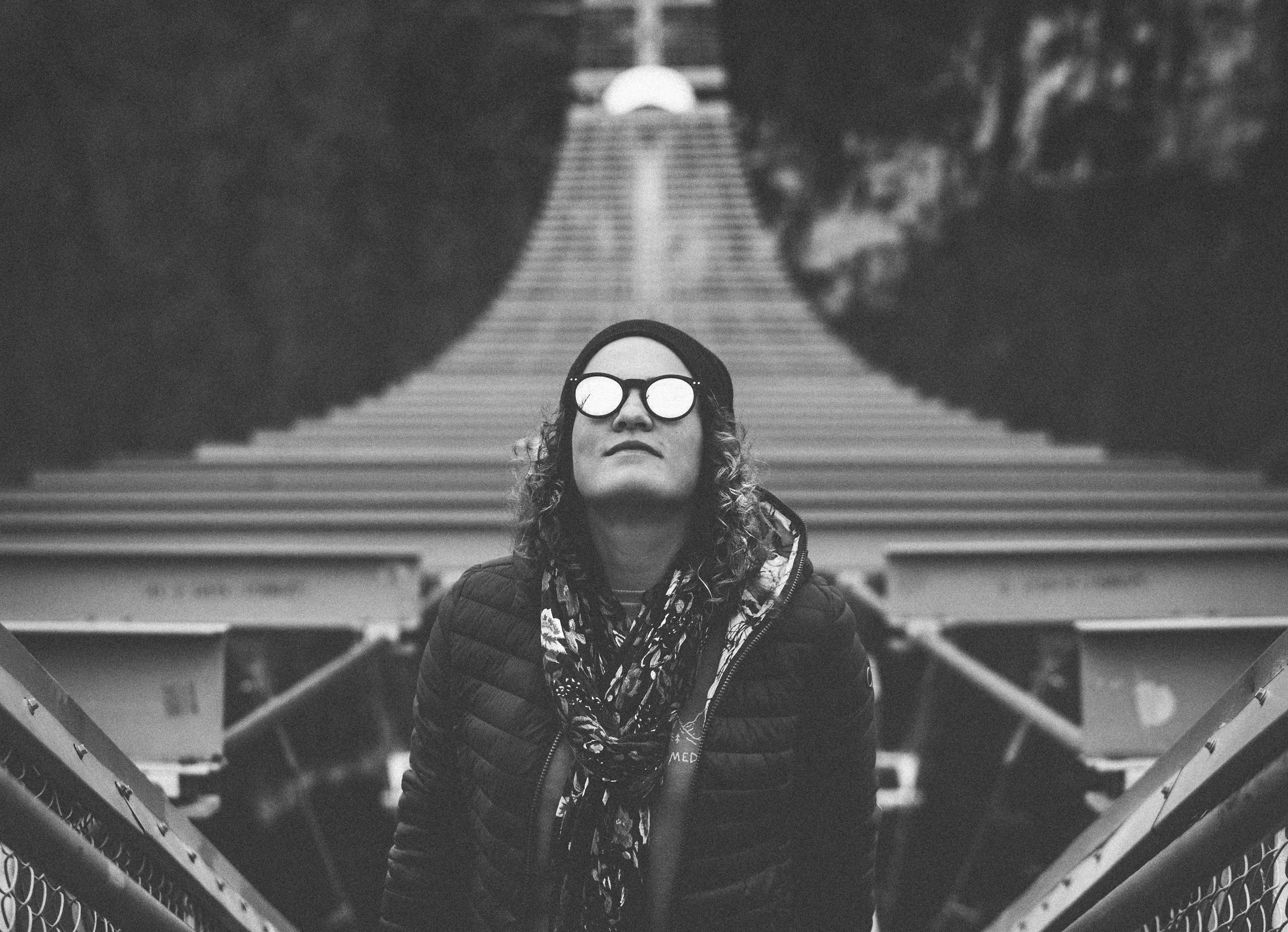 grayscale photography of woman standing while looking up on hanging bridge